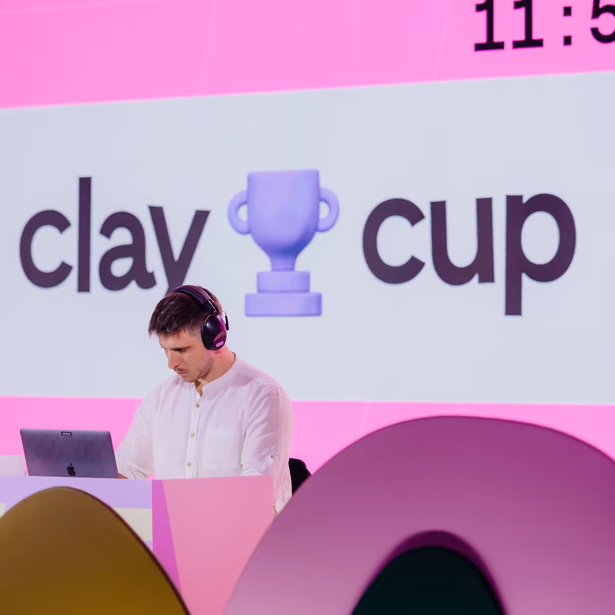 Man wearing headphones working on a laptop in front of a screen with 'clay cup' and a trophy emoji.